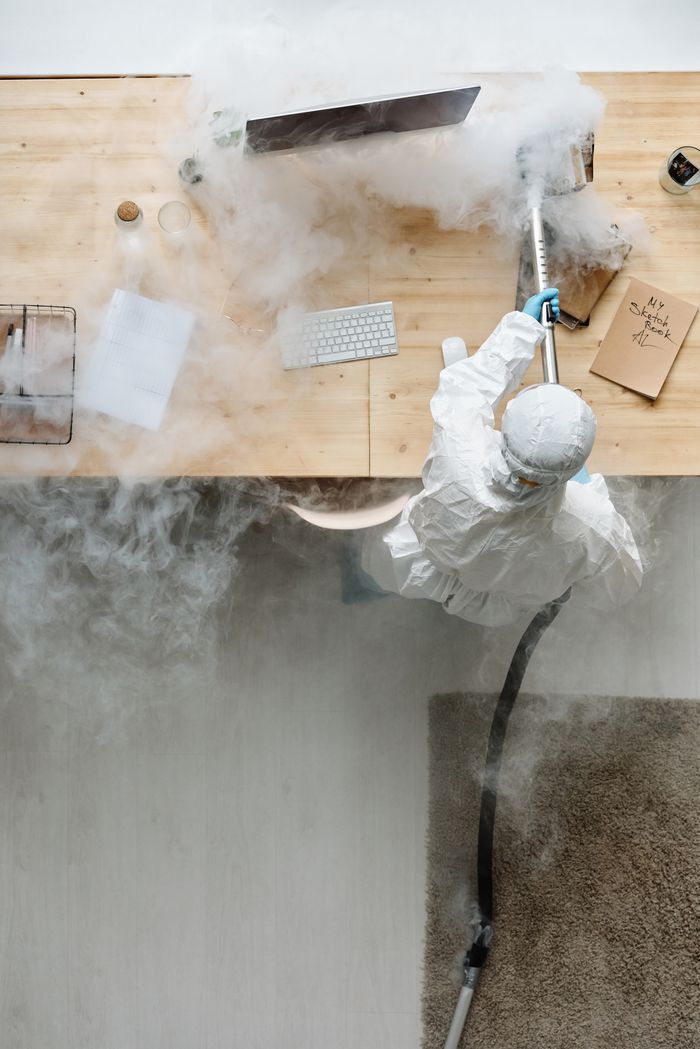 Une personne équipée de protections désinfectant un bureau à l’aide d’un appareil de fumigation en journée.