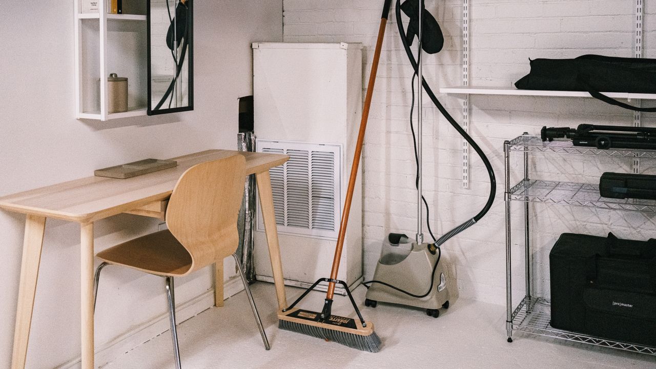A neat home office area with a wooden desk, chair, broom, and cleaning tools.